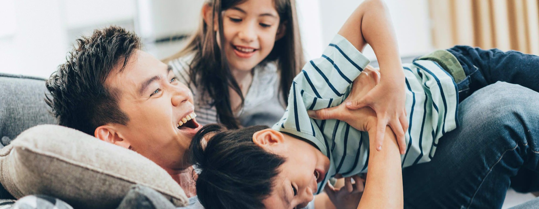 father plays on a couch with his young children